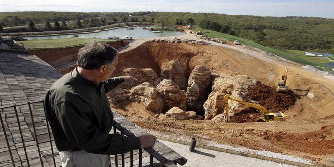 PLEASE HOLD FOR STORY SLUGGED HIDDEN CAVES BY JIM SALTER - In this photo made Thursday, April 14, 2016, Johnny Morris, founder of Bass Pro Shops, points to a massive sinkhole that opened up on his golf course during heavy rain last spring in Ridgedale, Mo. Experts urged Morris to fill the hole with clay and boulders, but he was intrigued by the possibility that an unknown cave system was at the root of the sinkhole which he believes could tie into other caves nearby including one he himself discovered over two decades ago.(AP Photo/Jeff Roberson)